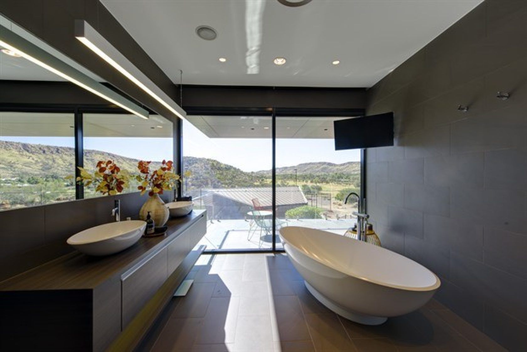 Modern bathroom with a white tub, dark gray walls, large windows, and a scenic outdoor view.