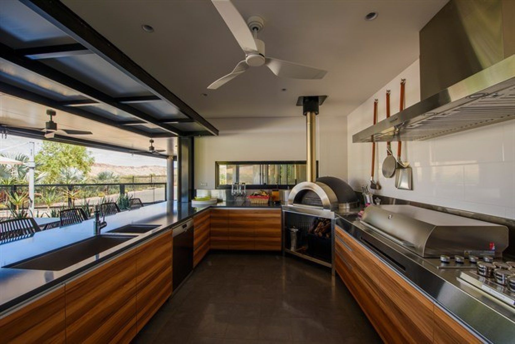 Outdoor kitchen with wood cabinets, pizza oven, grill, and open window.