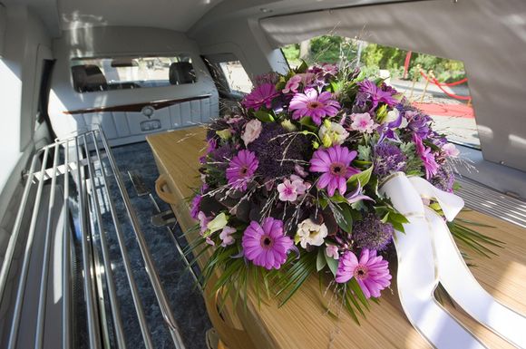 Una bara con fiori viola e un nastro bianco sopra