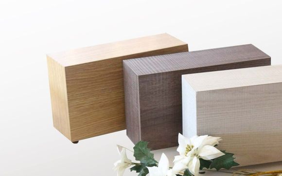 Tre urne cinerarie di legno sono posizionate una accanto all'altra su un tavolo.