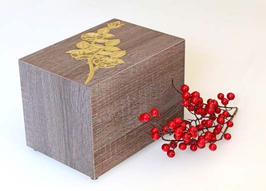 Urna cineraria in legno con un albero di Natale sopra è accanto a un mazzo di bacche rosse.