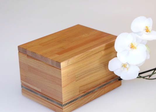 Urna cineraria in legno è posta accanto a un fiore bianco.
