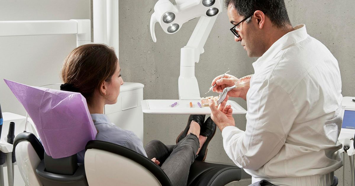 A woman is sitting in a dental chair talking to a dentist.