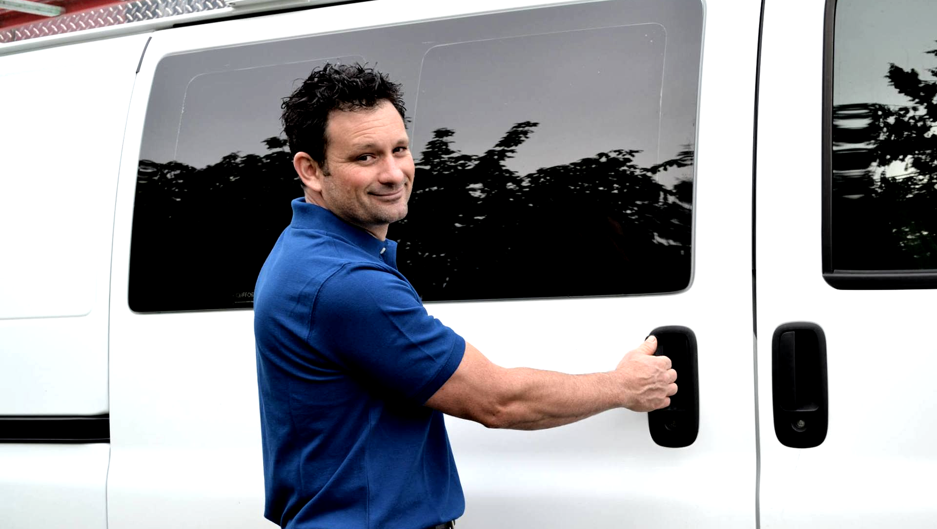 a man in a blue shirt is opening the door of a white van .