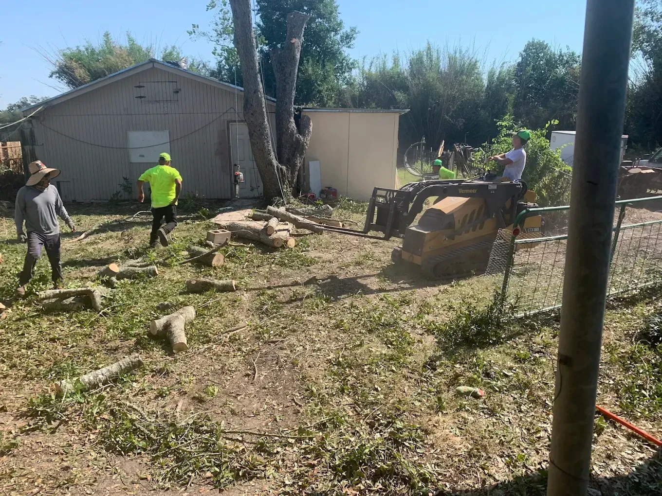 Men clearing debris with a small tractor and tools in a yard with a small building.