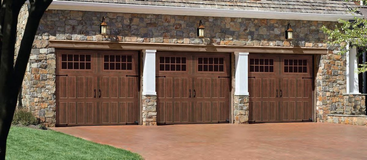 A house with three wooden garage doors and a brick driveway.