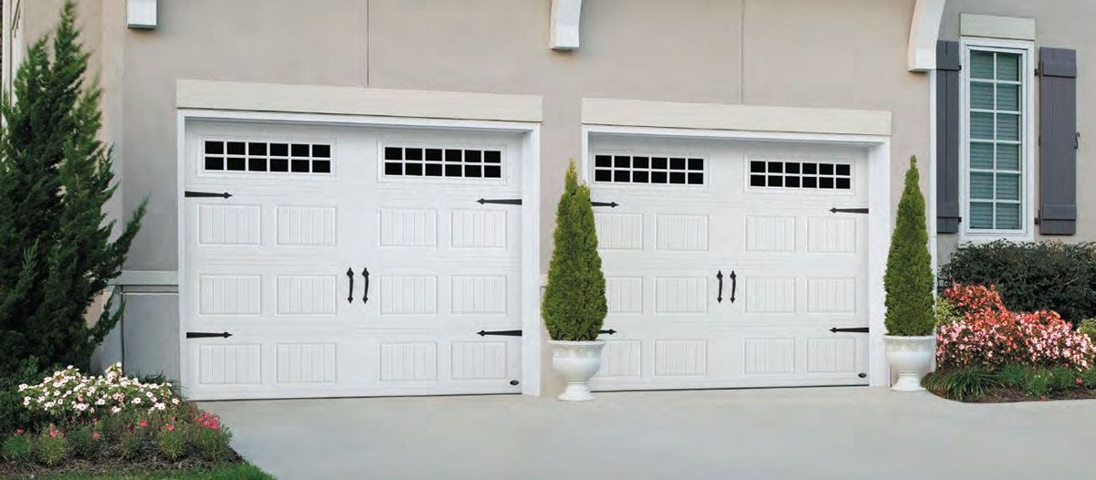 Two white garage doors are sitting next to each other in front of a house.