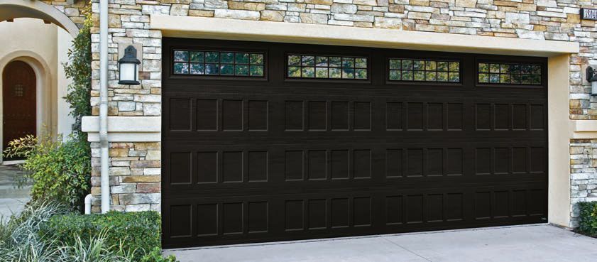 A large brown garage door is sitting in front of a stone house.