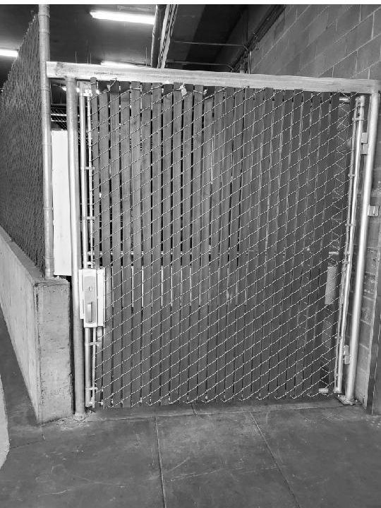 Chain link fence gate, secured. Industrial setting, metal frame, handle and locking mechanism visible.