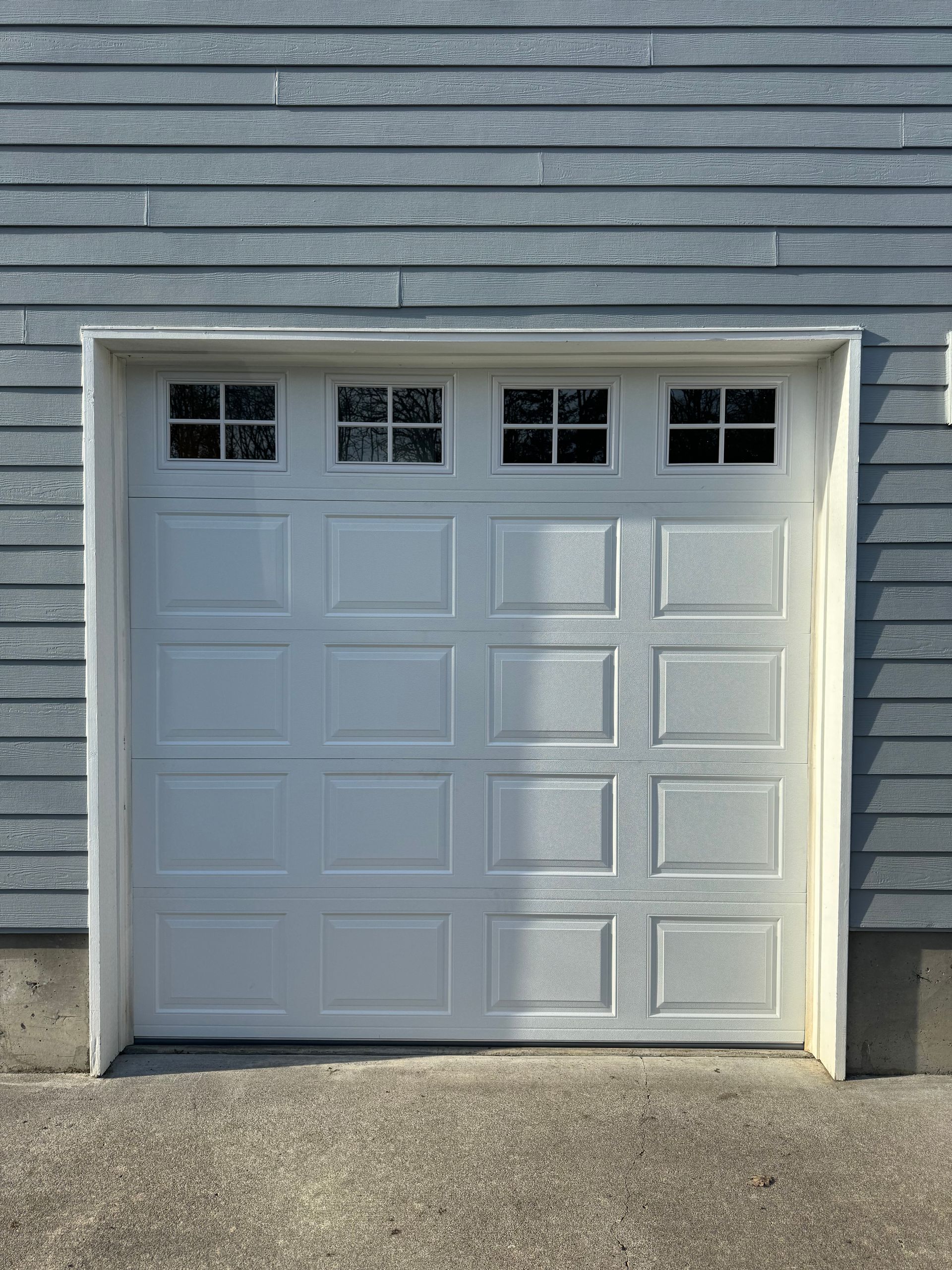 White garage door with four small square windows, set in a light blue building exterior.