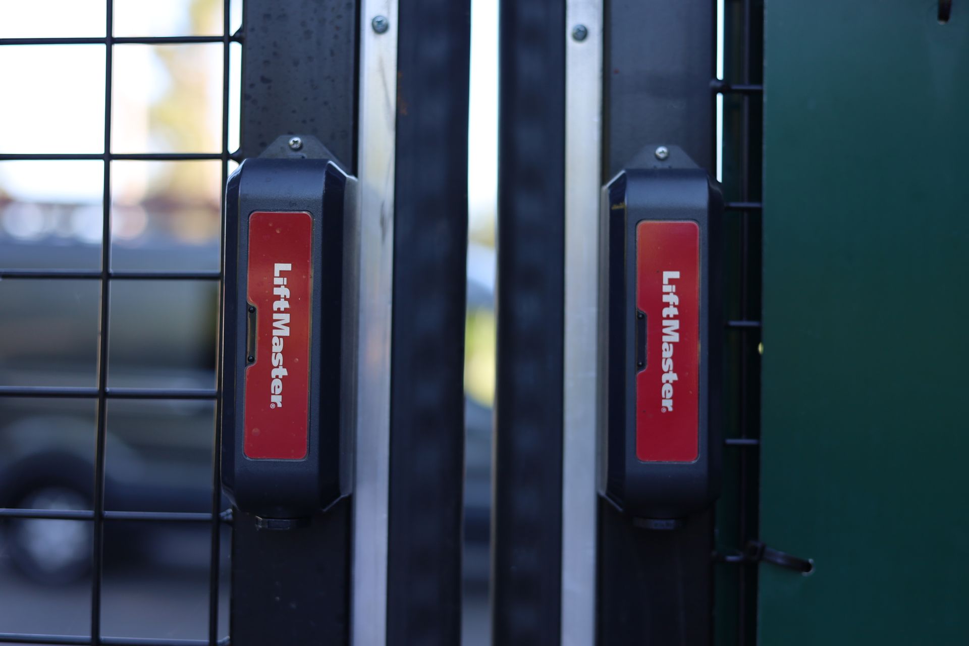 Two black LiftMaster gate openers mounted on a green metal gate.