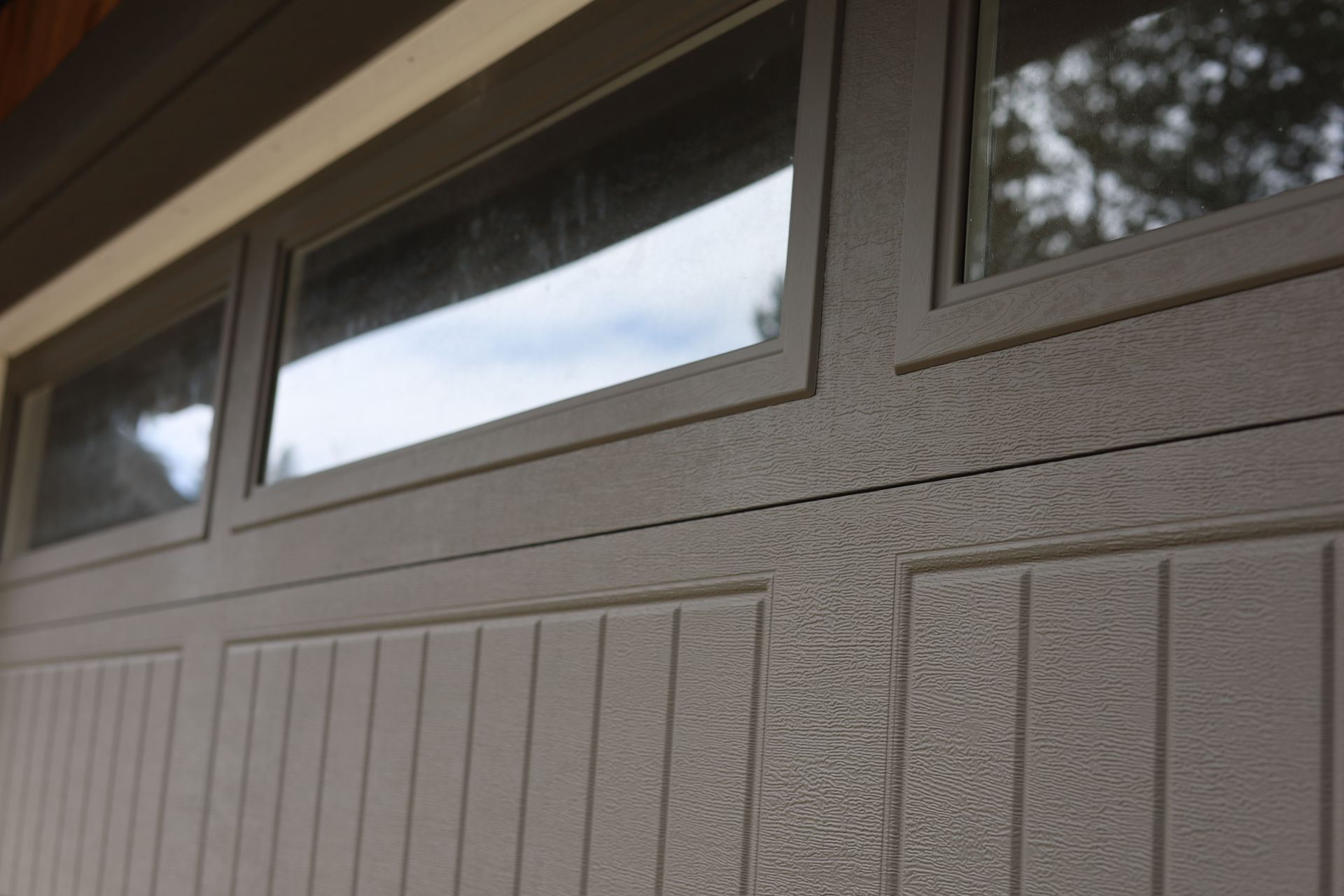 Beige garage door with three rectangular windows at the top.