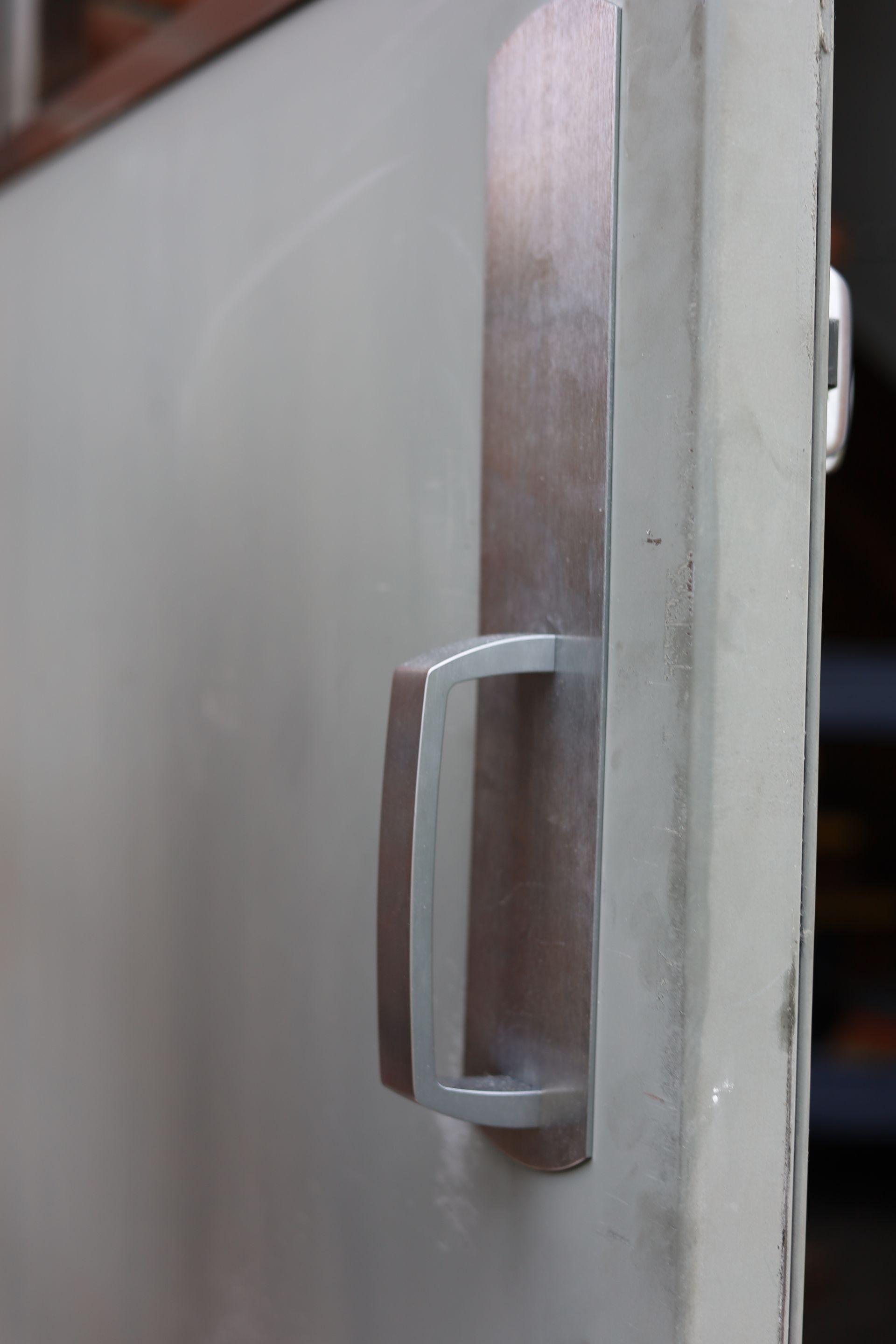 Metal door handle on a white door, close-up shot, with a rectangular back plate and a pull bar.