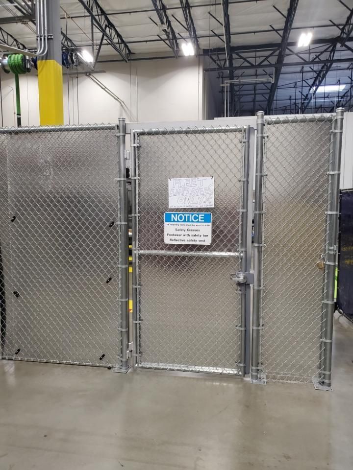 Metal chain-link fence with a gate inside a warehouse. 