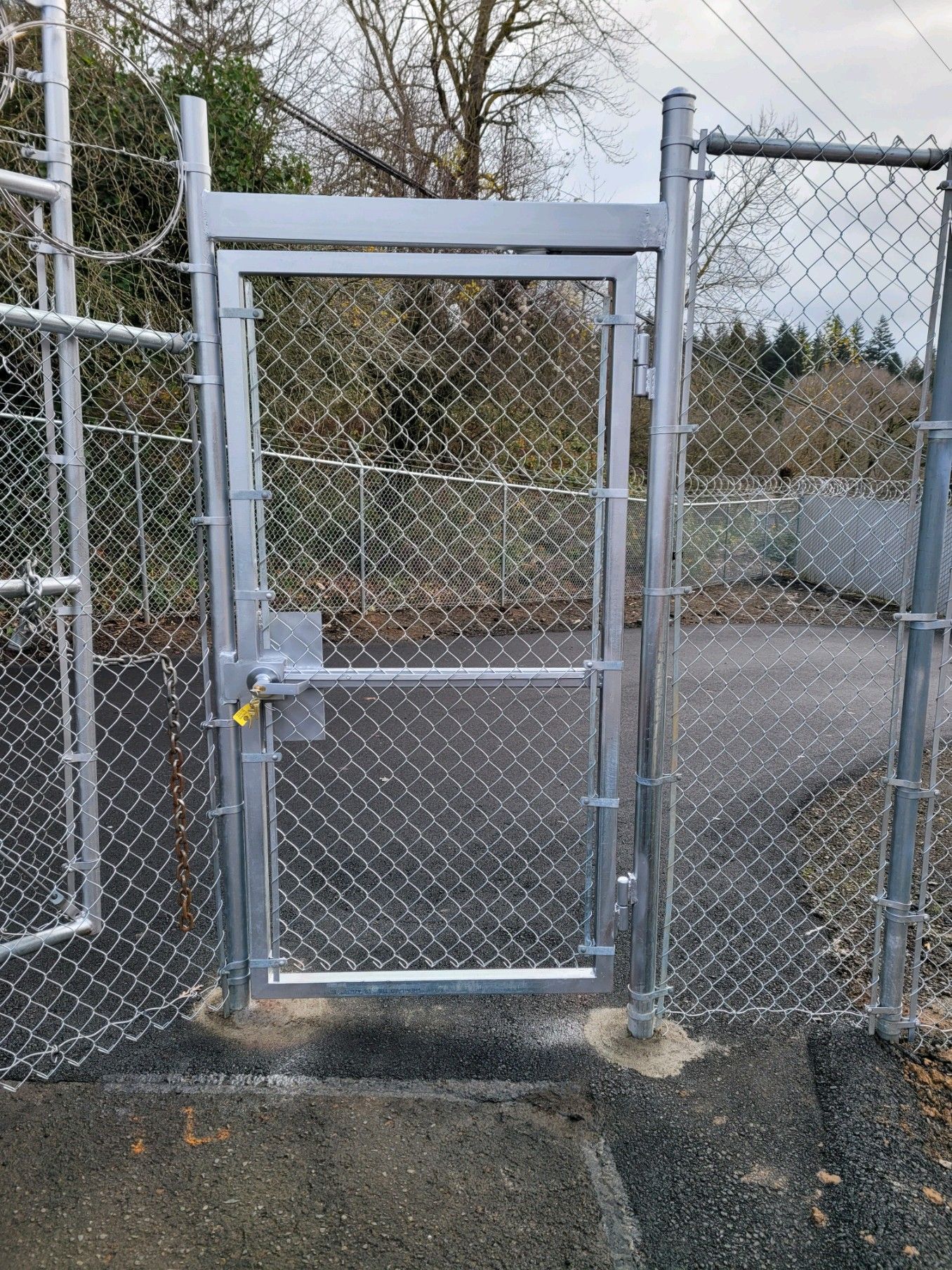 A chain-link fence gate is locked. Gray metal frame and chain link. Daytime outdoors.