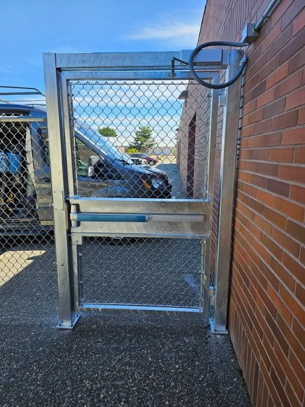 Metal gate with chain link fence, mounted on brick building and asphalt ground, blue sky background.