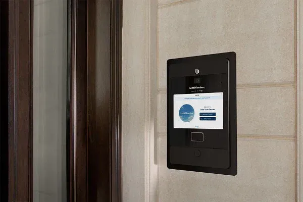 Black access control panel with a screen, mounted on a beige wall, next to a brown door frame.