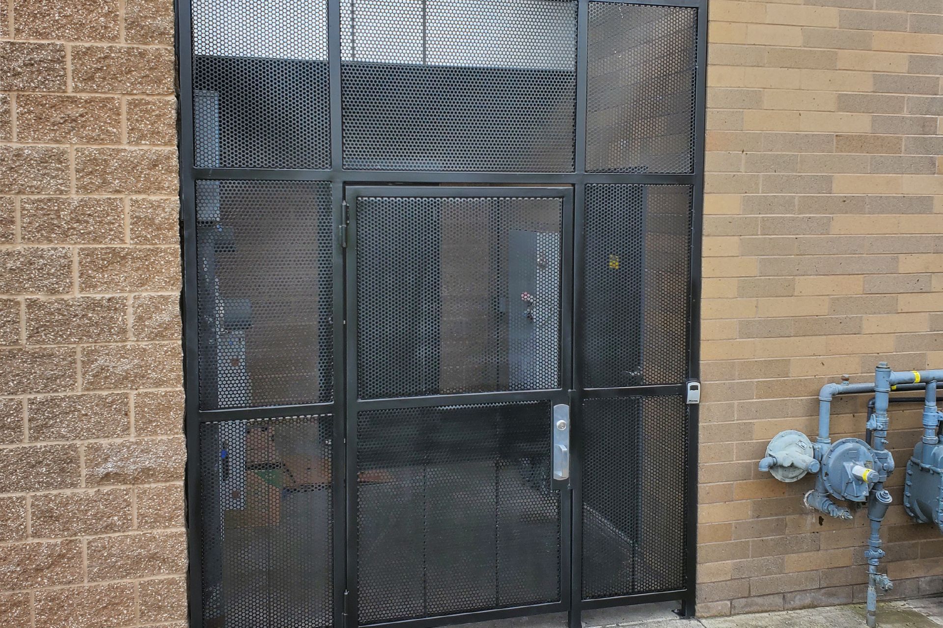 A metal gate is sitting on the side of a brick building.