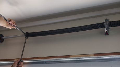Person using a winding bar to adjust a garage door spring, mounted on the ceiling.