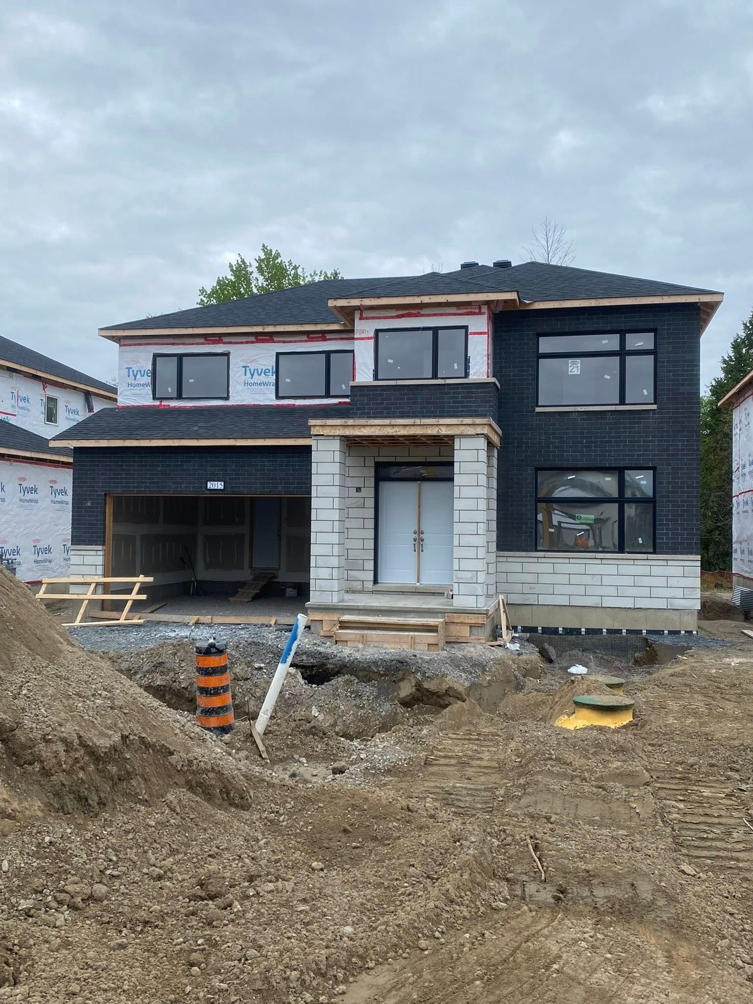 Maison en construction, bardage noir, toiture grise, à deux étages, terre devant, ciel nuageux.