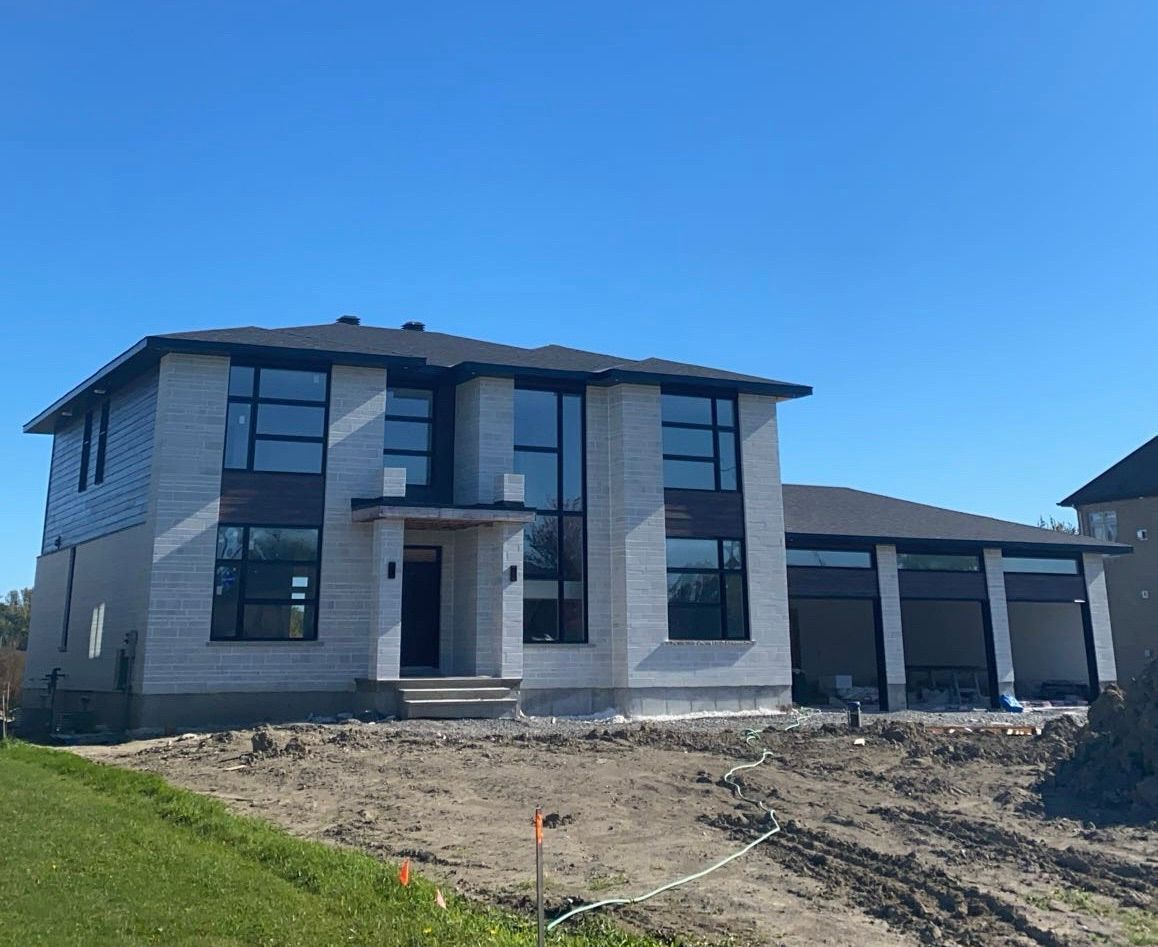 Maison moderne à deux étages en construction avec de grandes fenêtres et un ciel bleu.