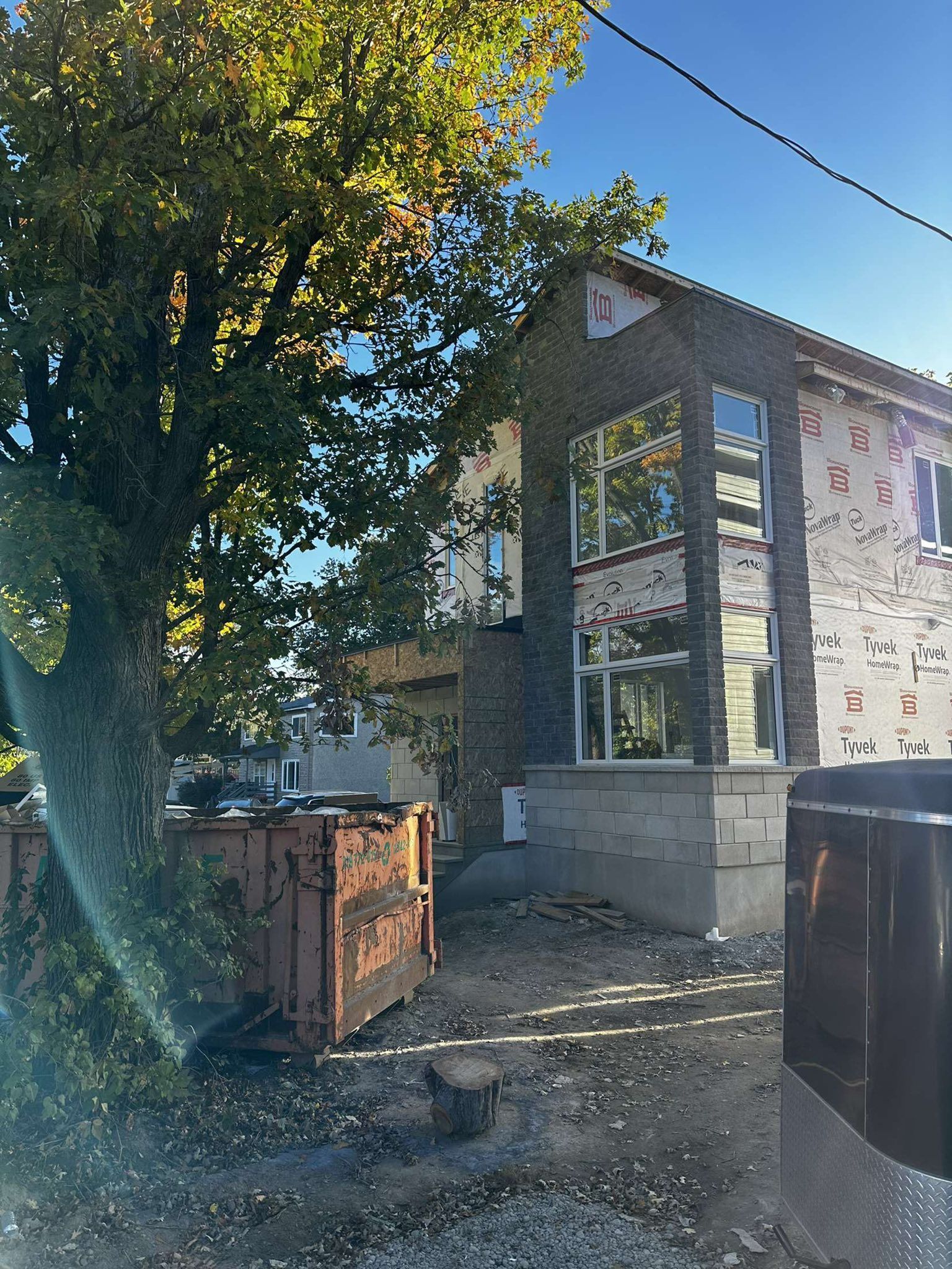 Chantier : bâtiment en briques avec grandes fenêtres, débris et arbre.