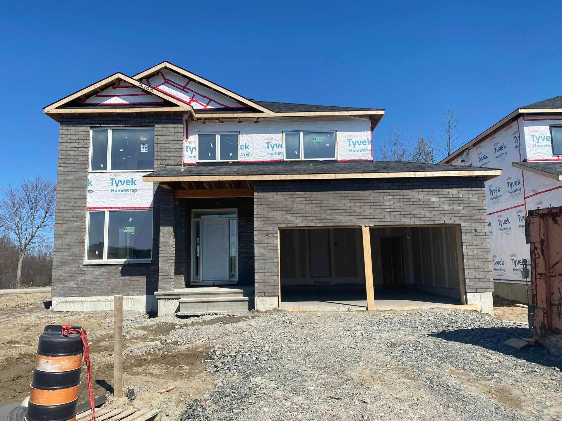 Nouvelle maison à deux étages en construction avec revêtement en pierre grise, garage pour deux voitures et ciel bleu.