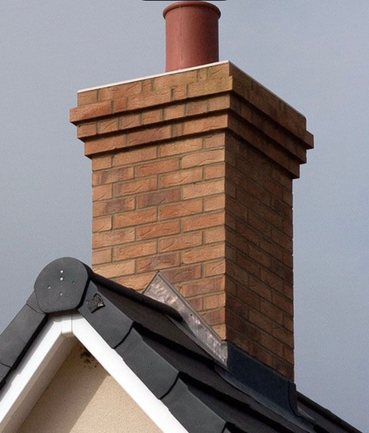 Cheminée en briques avec un pot en terre cuite au sommet, sur fond de ciel gris.