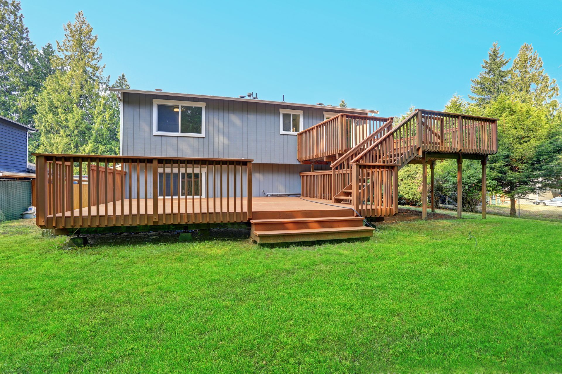 Back of a gray house with two wooden decks and stairs on a green lawn.