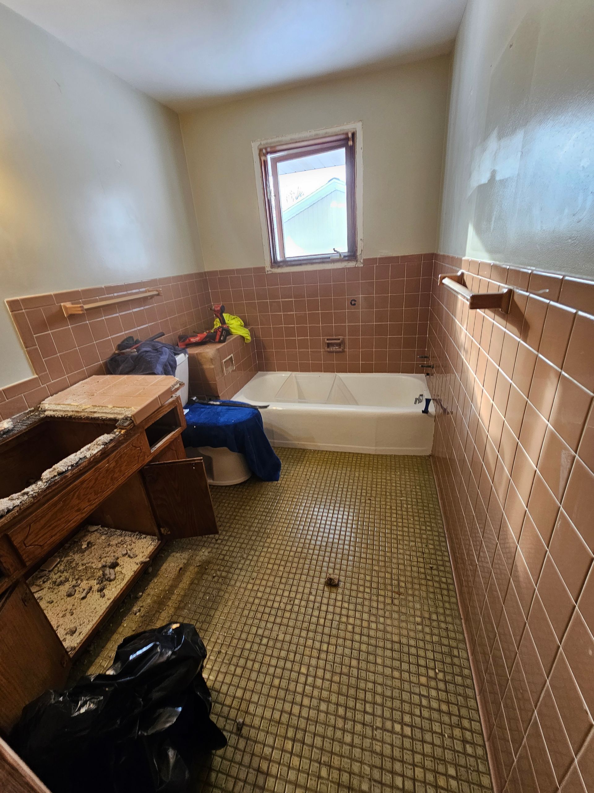 Bathroom with brown tiled walls, small window, and tub. The floor has patterned tiles.
