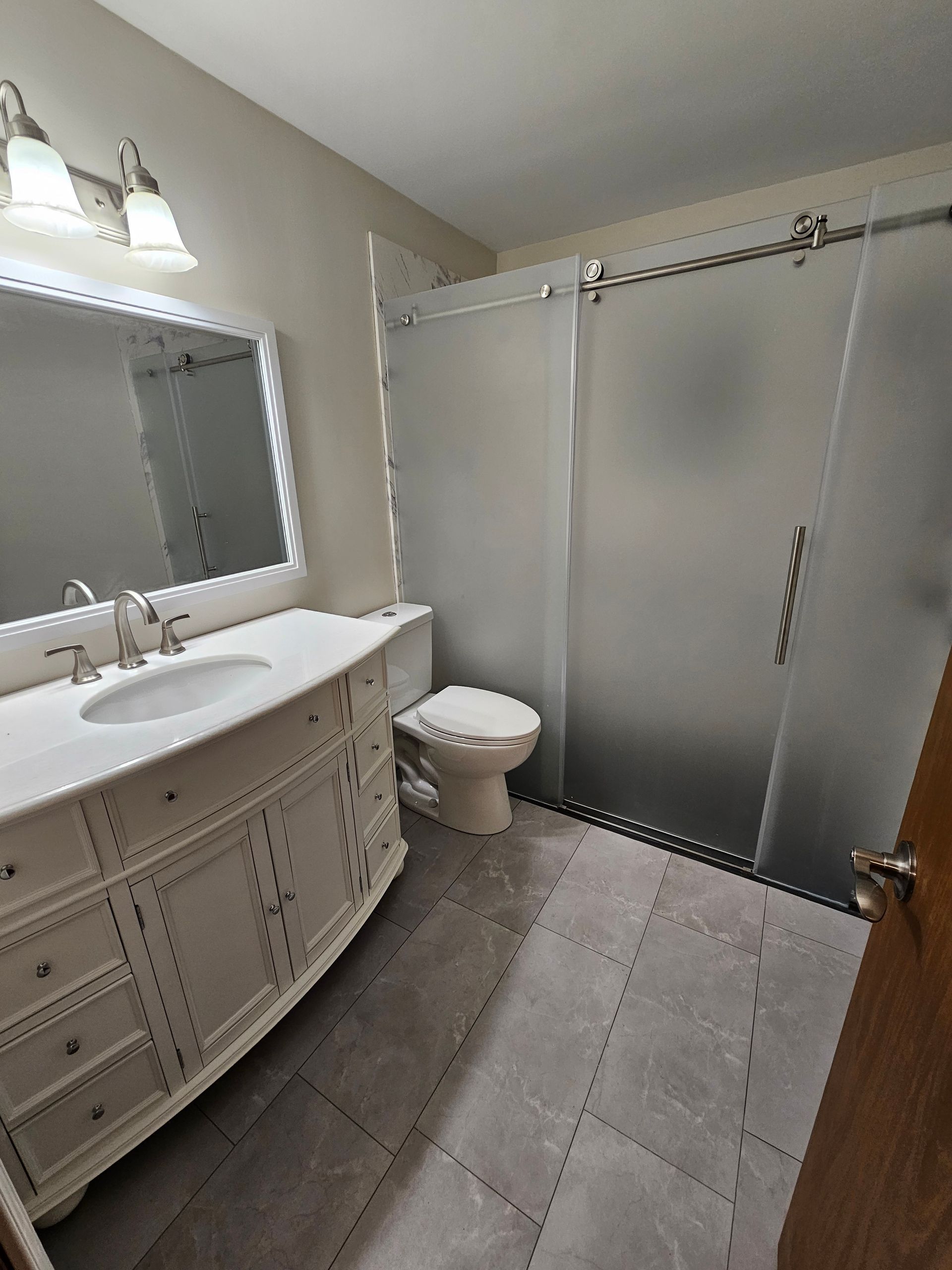 Bathroom with white vanity, frosted glass shower door, and gray tiled floor.