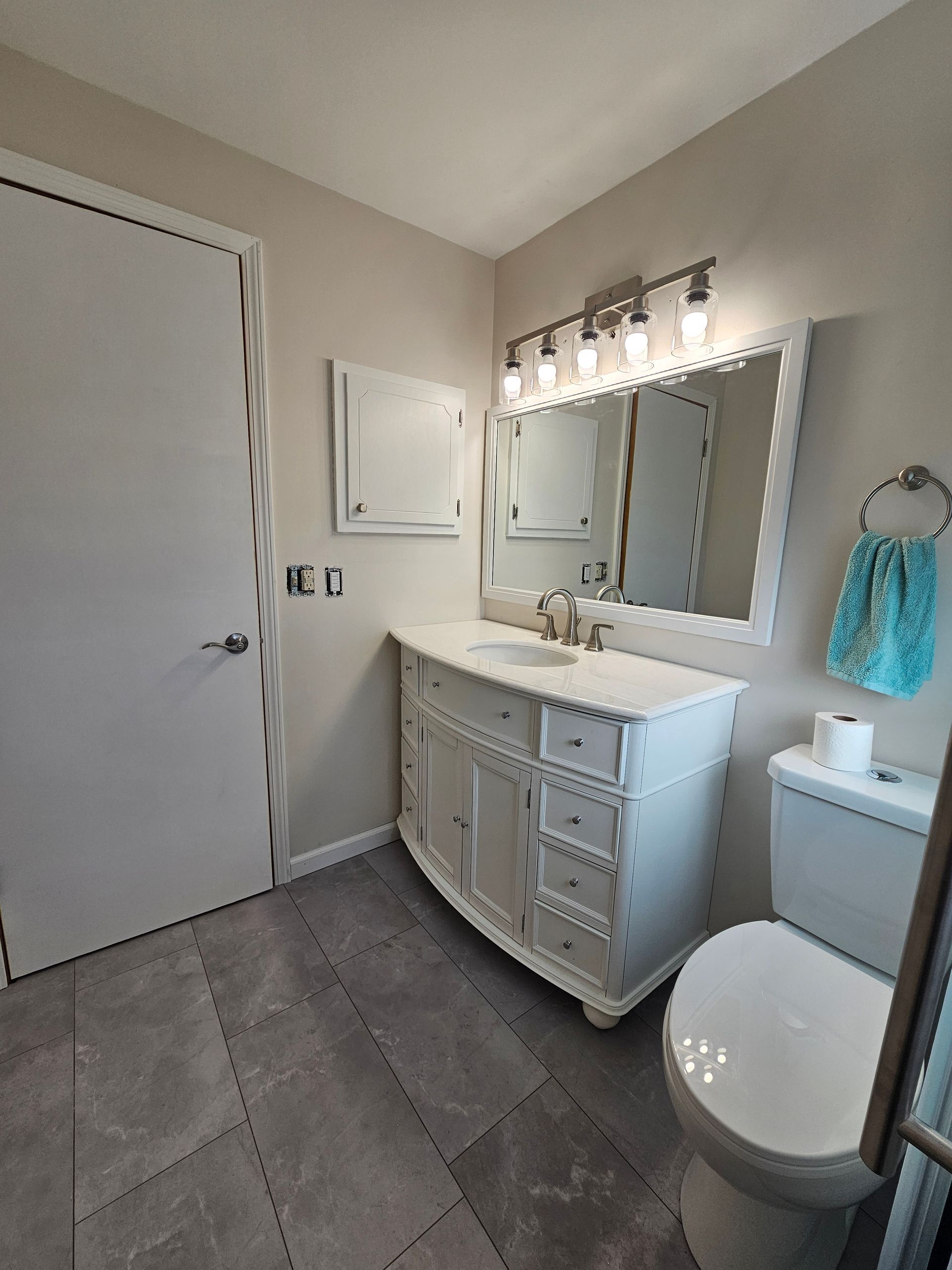 Bathroom with white vanity, toilet, mirror, and towel rack. Gray tiled floor and light-colored walls.