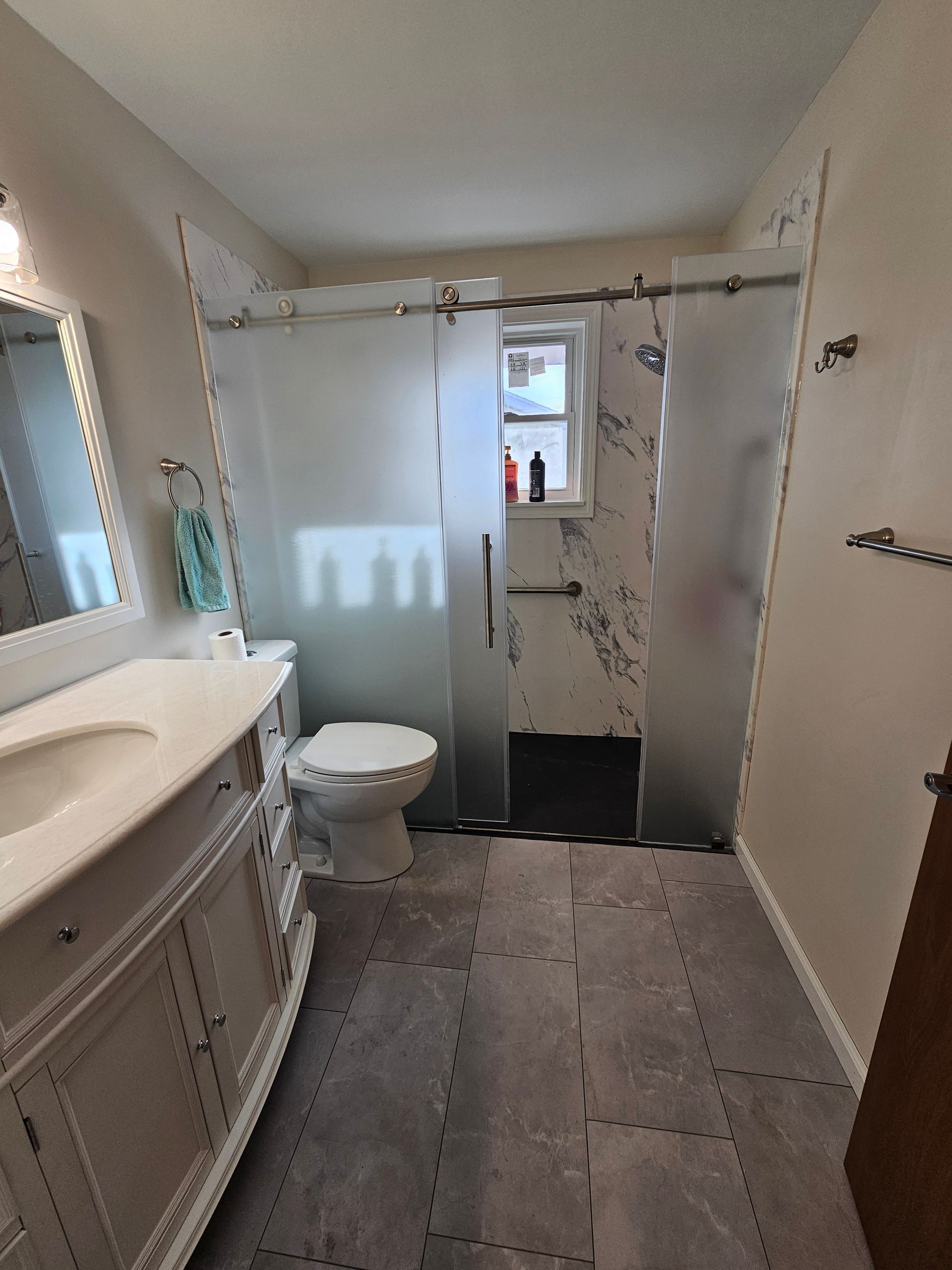 Bathroom with a vanity, toilet, and a frosted glass shower enclosure. Gray tiled floor.
