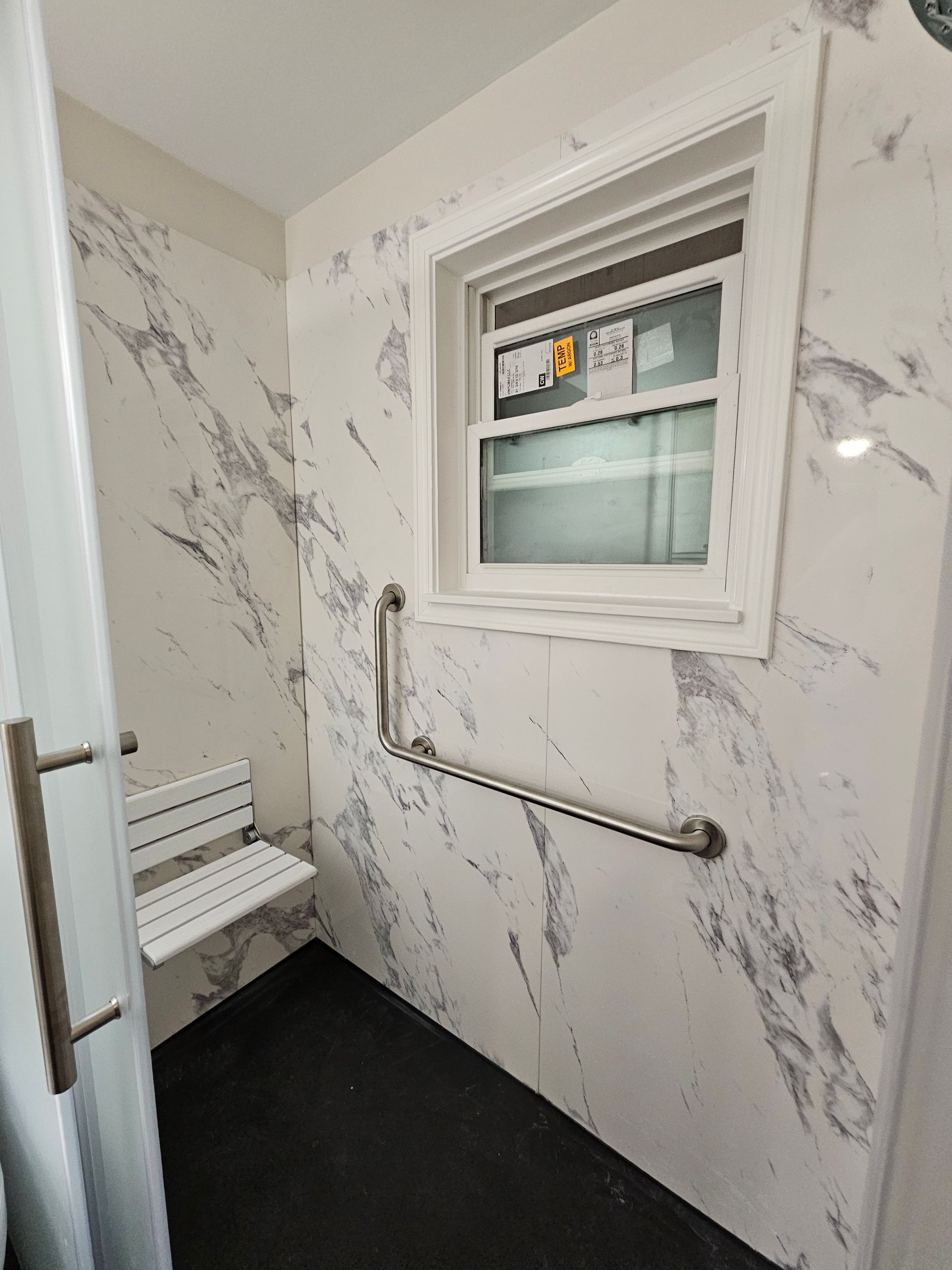Accessible shower with a seat, grab bar, and window. Marble-look walls, black floor.