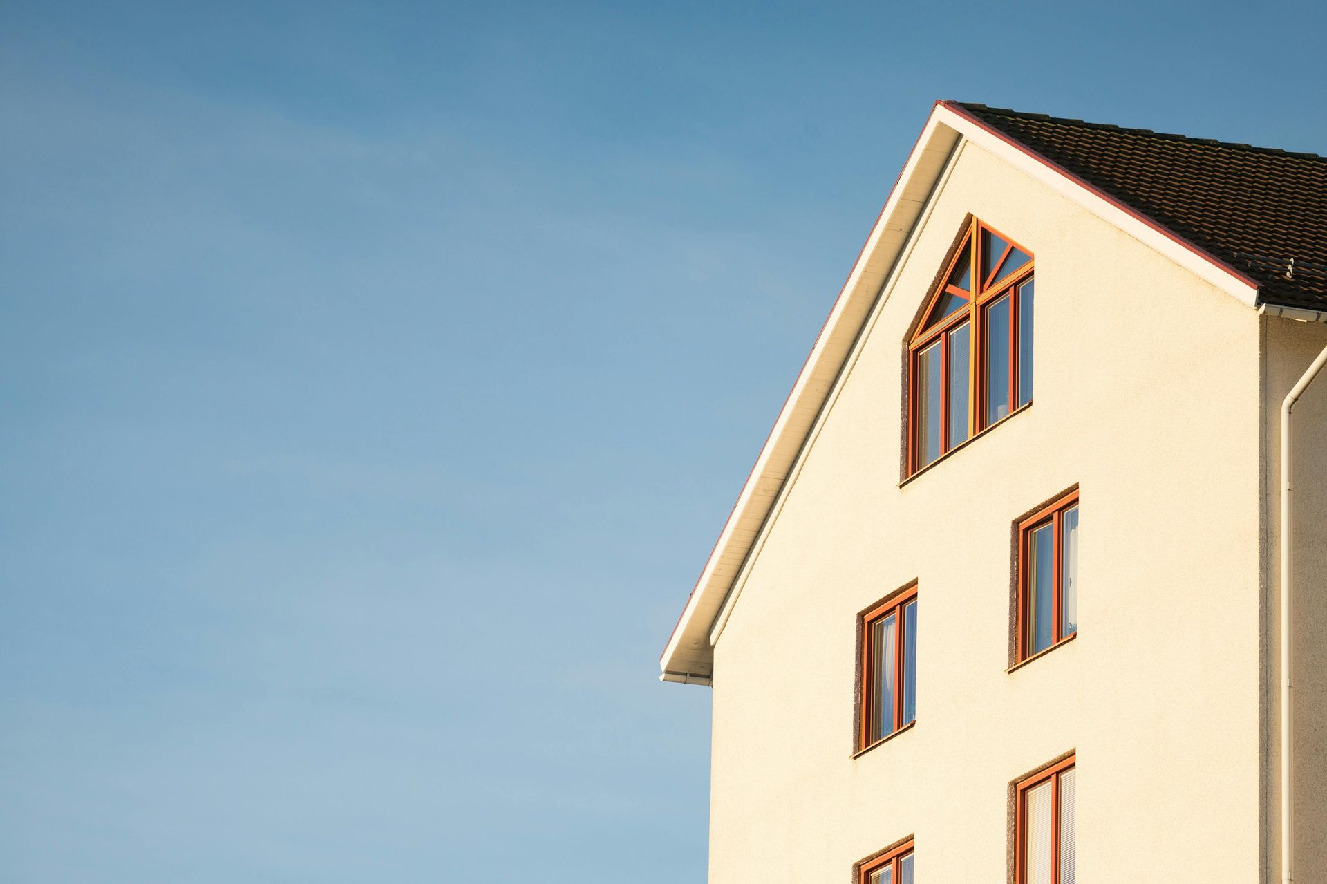White house with a triangular window and brown roof against a clear blue sky.
