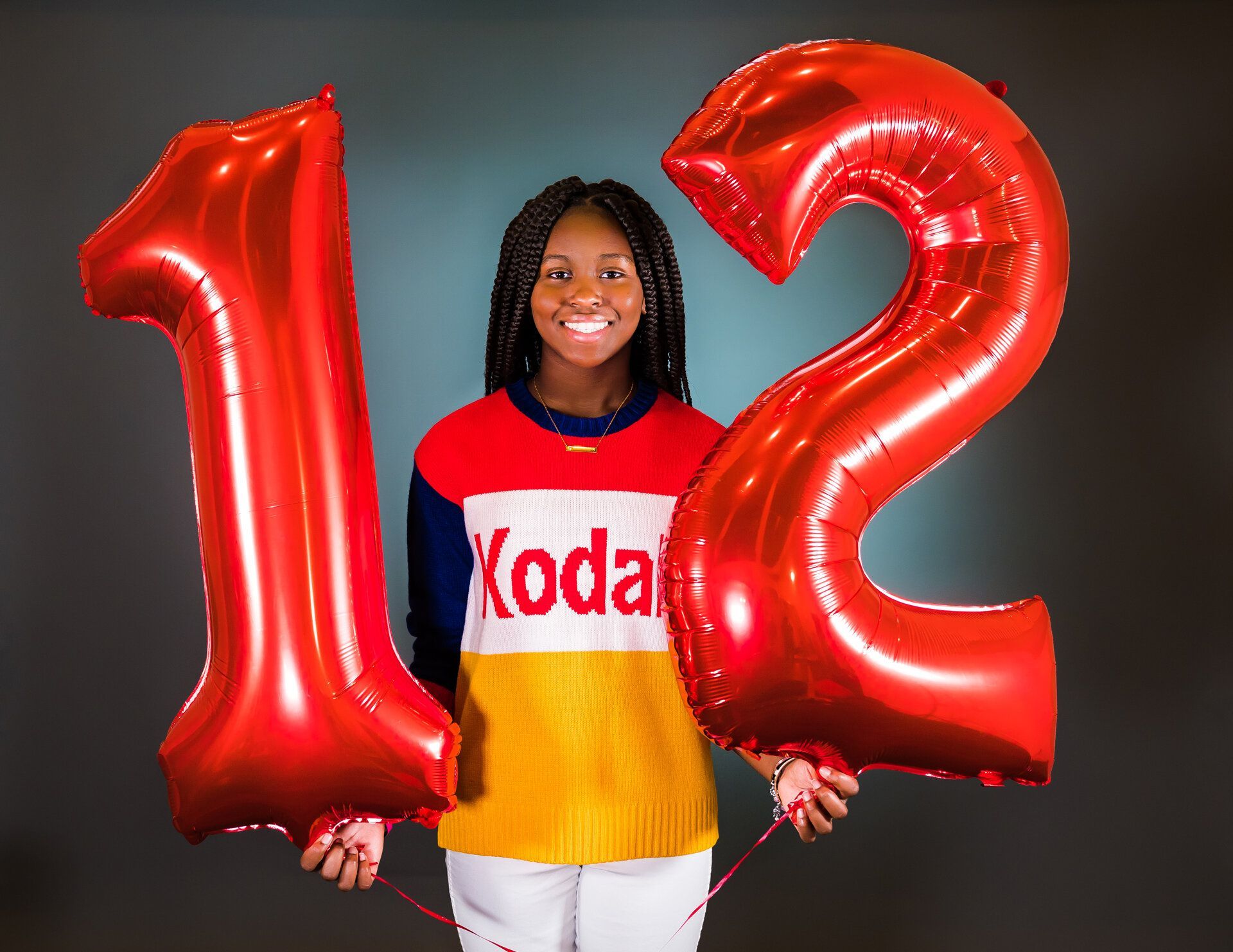 A woman is holding red balloons in the shape of the number 12.