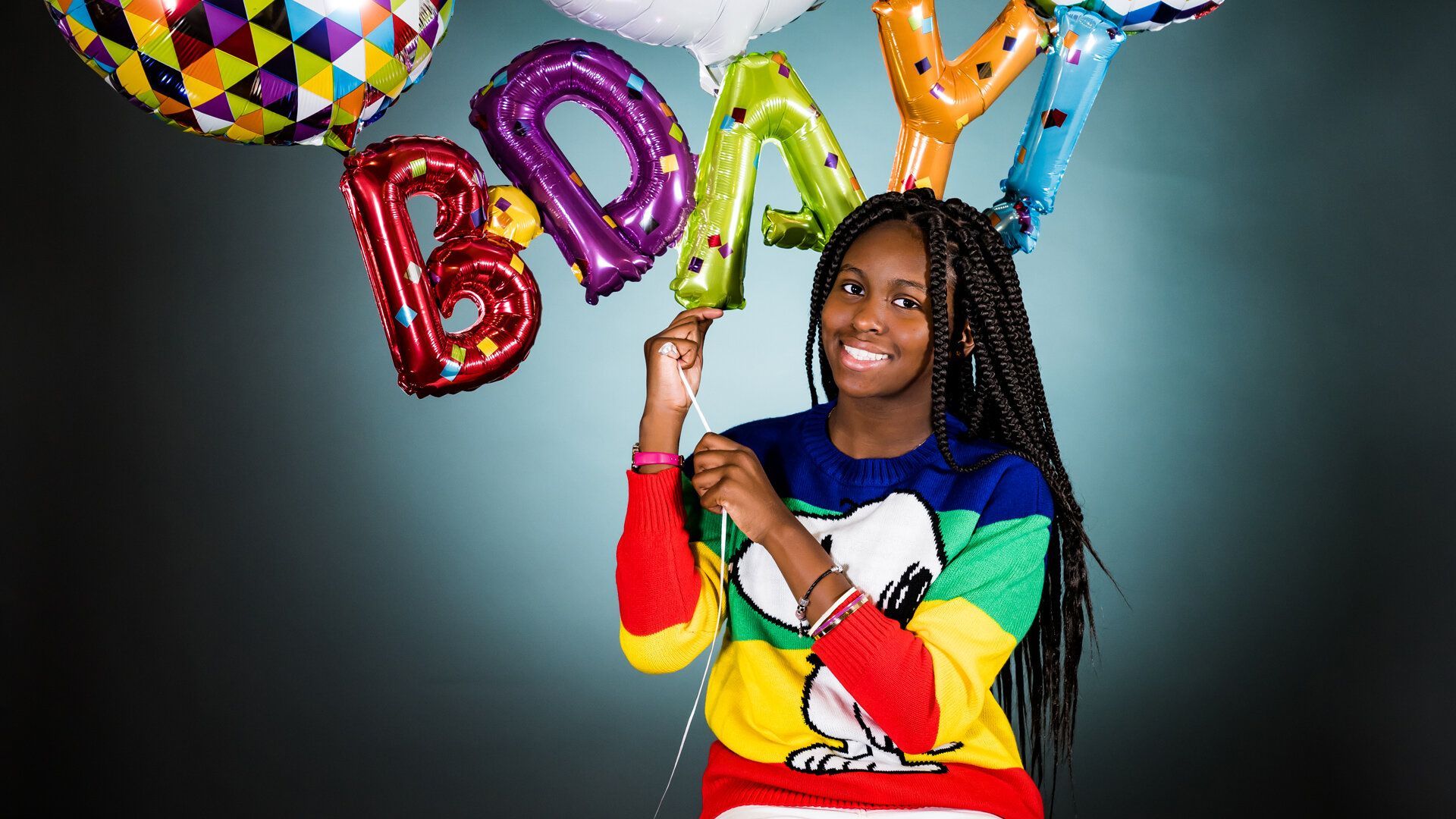 A young girl is holding a bunch of birthday balloons.