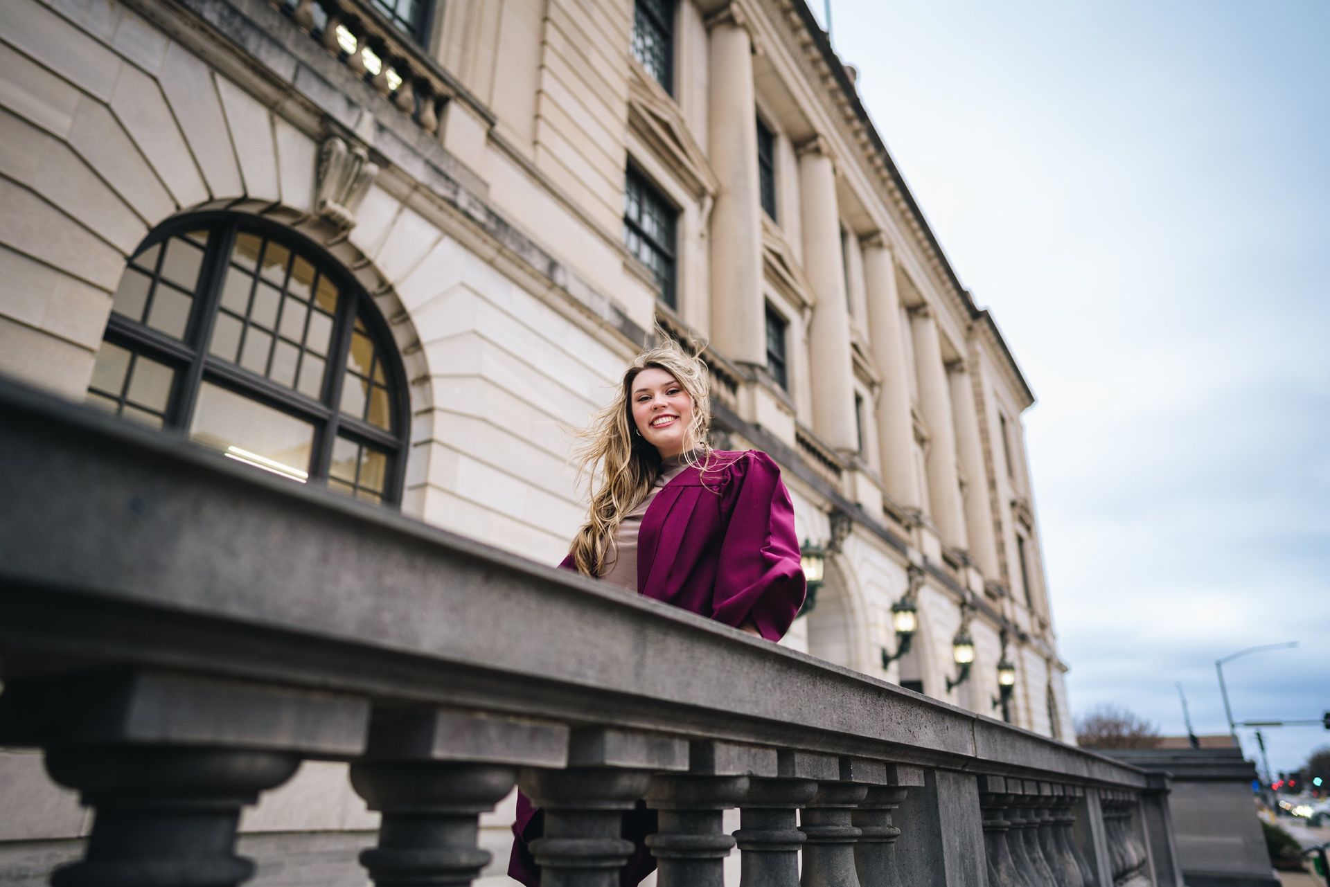 A woman in a cap and gown is standing on a balcony in front of a building.