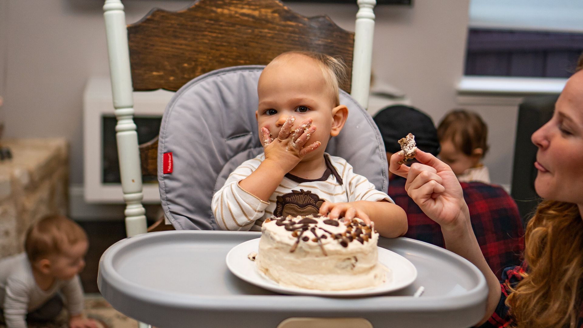 A baby is sitting in a high chair eating a piece of cake.