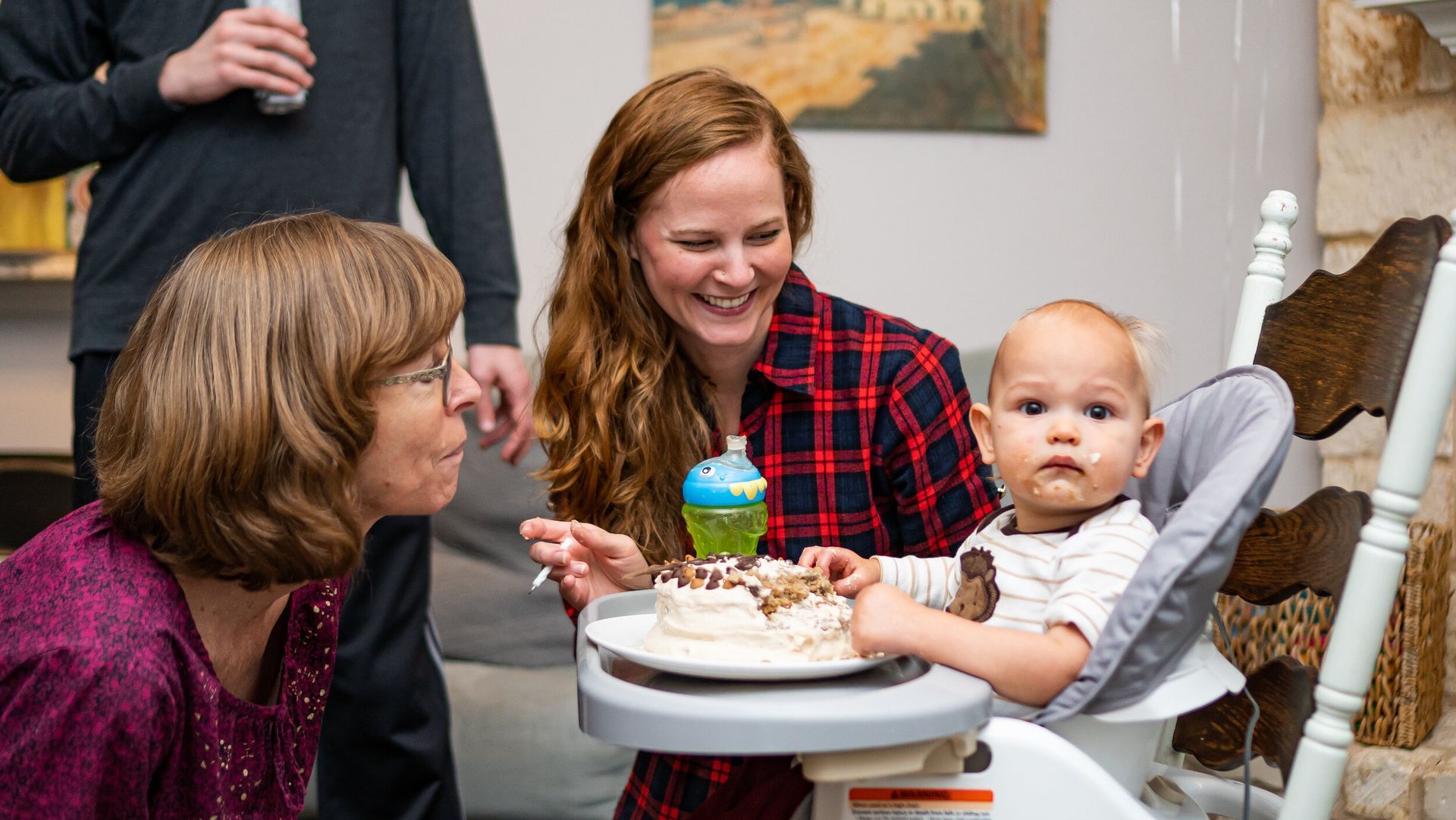 A baby is sitting in a high chair eating a birthday cake.