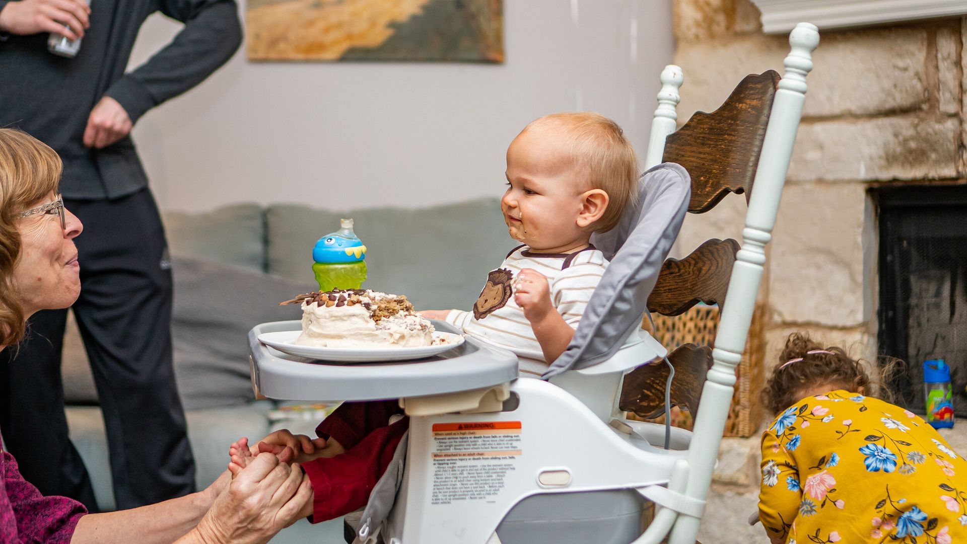 A baby is sitting in a high chair eating a cake.
