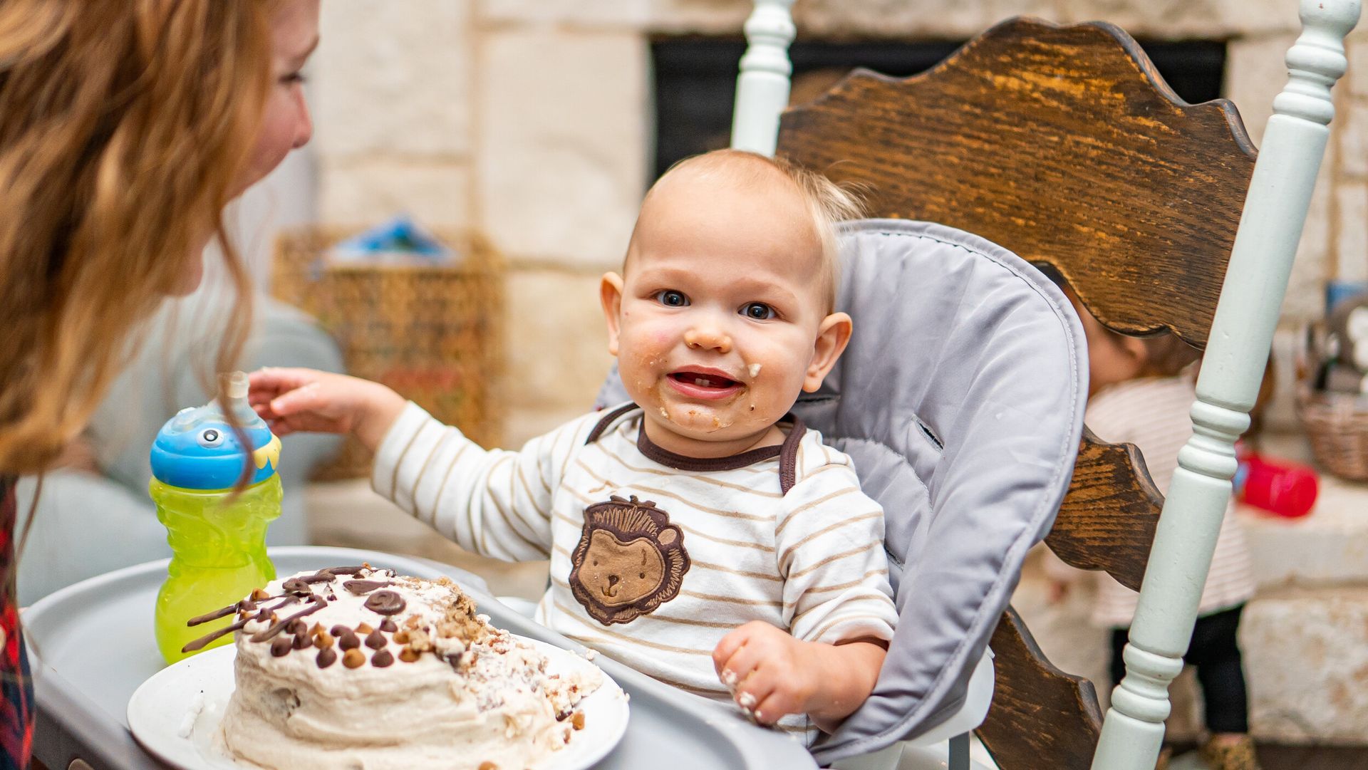 A baby is sitting in a high chair eating a cake.