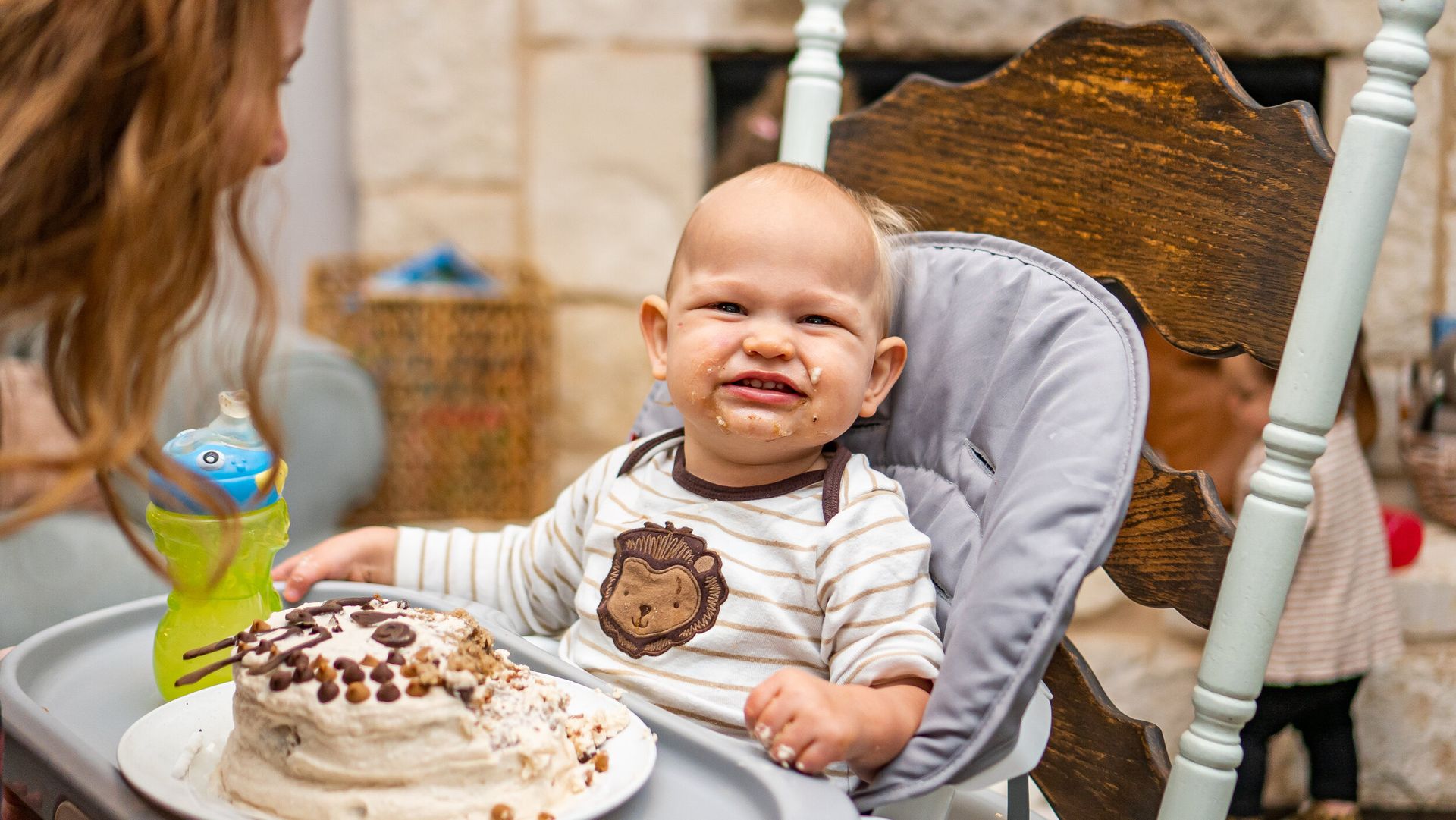 A baby is sitting in a high chair eating a cake.