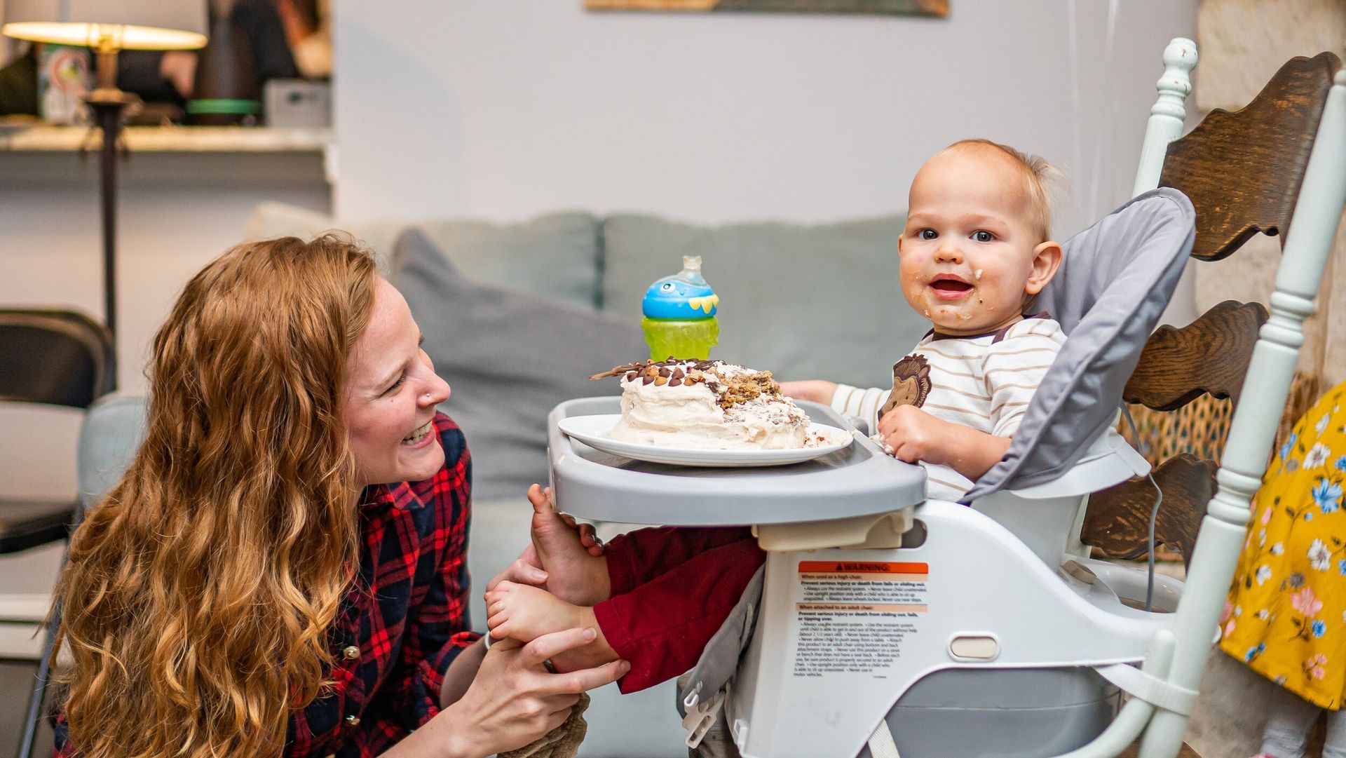 A woman is sitting next to a baby in a high chair.