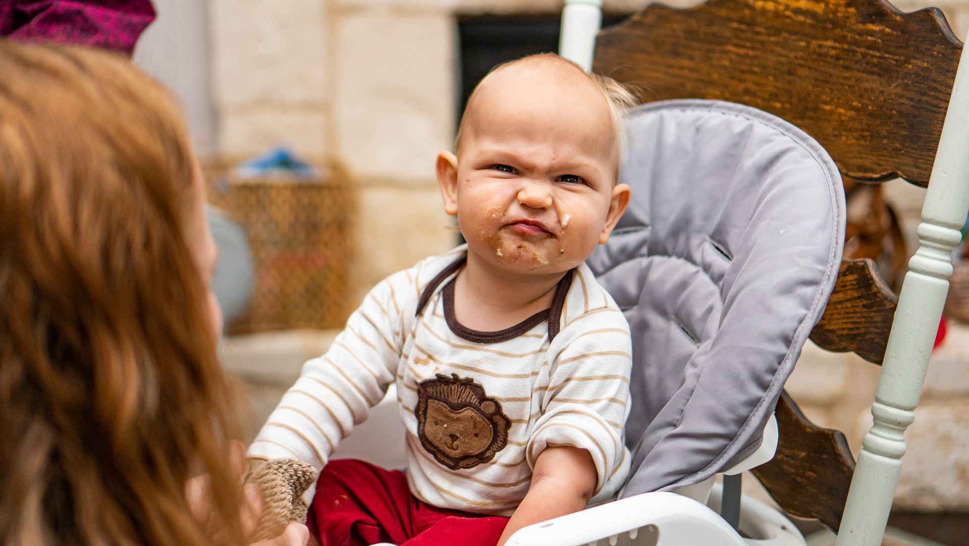 A baby is sitting in a high chair making a funny face.