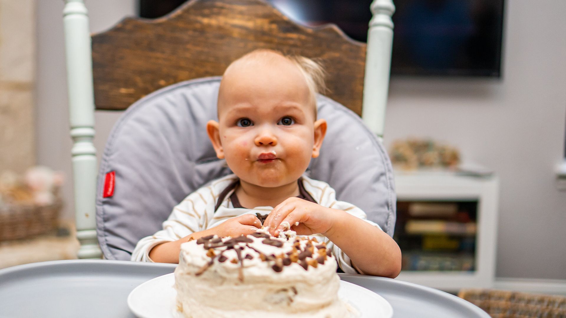 A baby is sitting in a high chair eating a birthday cake.