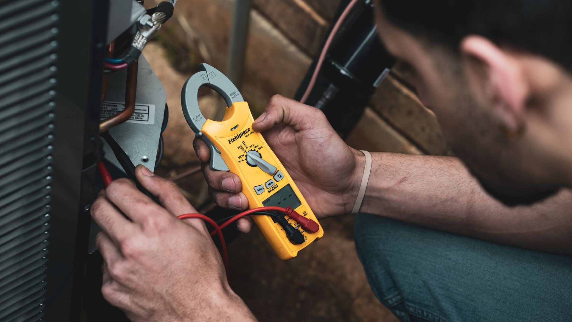 A man is working on an air conditioner with a clamp meter.