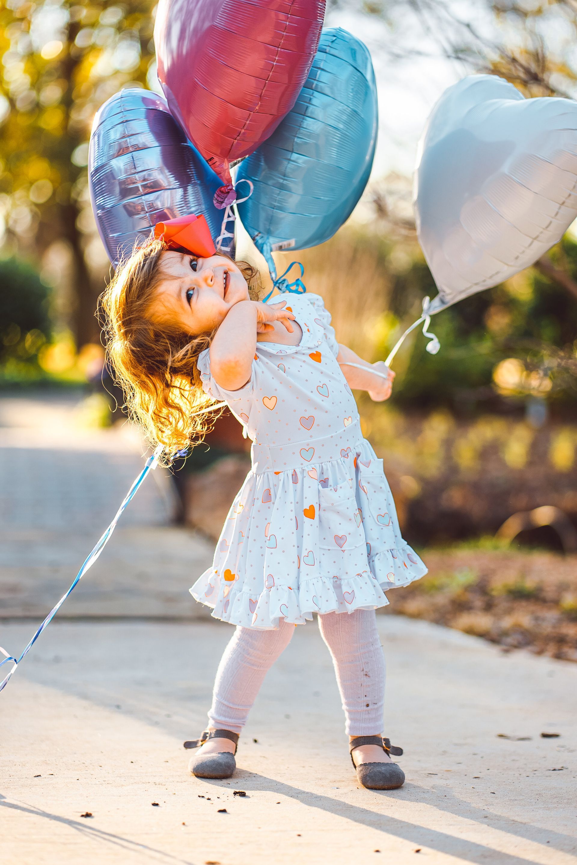A little girl is holding a bunch of balloons in her hands.