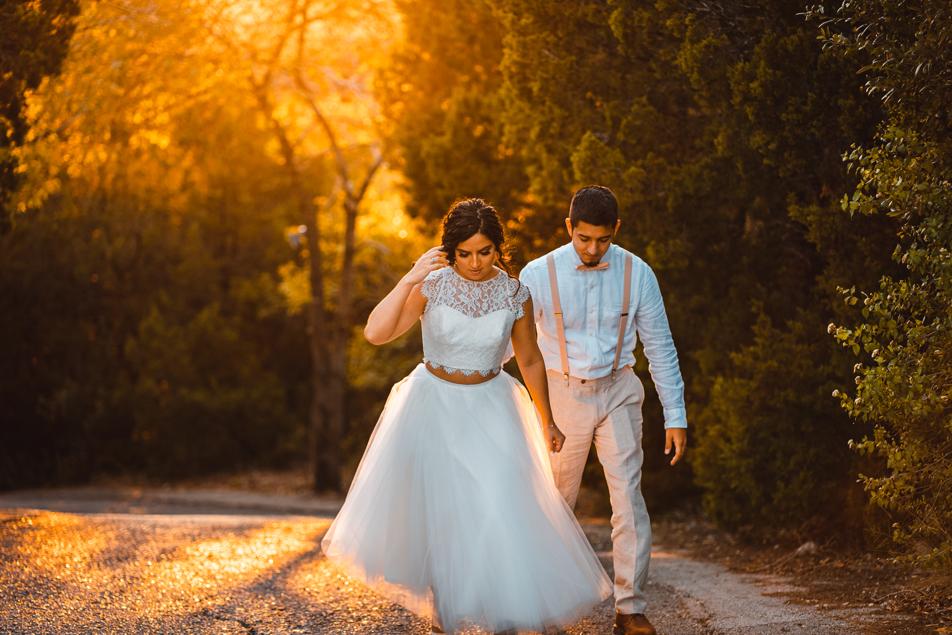 A bride and groom are walking down a dirt road holding hands.