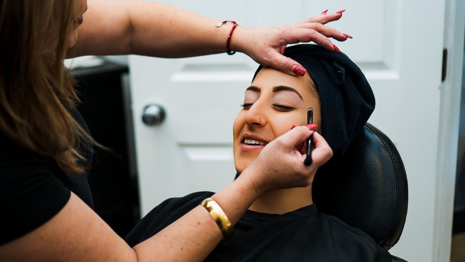 A woman is getting her eyebrows done by a makeup artist.